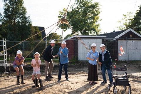 Bewoners en bestuurders slaan samen symbolisch de eerste paal om de bouwstart officieel in te luiden. 